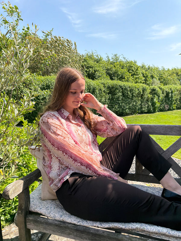 Woman sitting on a bench in a garden with greenery and blue sky.
